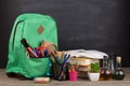 Education concept - school backpack with books and other supplies, blackboard background Royalty Free Stock Photo