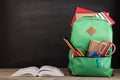 Education concept - school backpack with books and other supplies, blackboard background