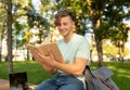 Education concept. Teenage student guy reading book outdoors and preparing for exams, sitting in campus Royalty Free Stock Photo