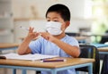 Education, covid and learning with face mask on boy doing school work in classroom, writing and counting at his desk in Royalty Free Stock Photo