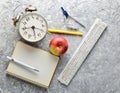 Education equipment. Alarm clock, notepad, ruler, apple, pen, compasses on a gray concrete background. Top view, flat lay style.