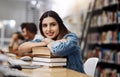 Education gives you endless possibilities in life. a young woman resting on a pile of books in a college library and