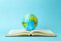 Education and globalism concept. Globe on an open book on a table in a university class on a blue background