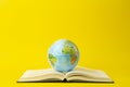 Education and globalism concept. Globe on an open book on a table in a university class on a yellow background