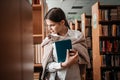 education, high school, university, learning concept - smiling student girl reading book at library