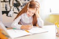 Education at home concept - Cute little girl with long hair studying or completing home work on a table with pile of books and