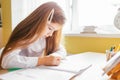 Education at home concept - Cute little girl with long hair studying or completing home work on a table with pile of books and