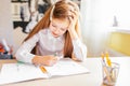 Education at home concept - Cute little girl with long hair studying or completing home work on a table with pile of books and