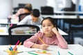 Bored asian school girl sitting at desk in classroom