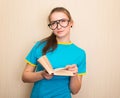 Education and school concept. Dreamy teen girl student in eyeglasses reading a book standing against white wall