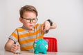 Education, school, finance, money and happiness concept smiling smart kid boy counting money with piggy bank at table at Royalty Free Stock Photo