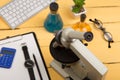 Education and science concept - microscope, book, magnifying glass, calculator, watch, blank clipboard, computer keyboard, eyeglas