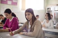 Teenagers students sitting in the classroom and writing. Girl looking at camera. Focus is on foreground Royalty Free Stock Photo