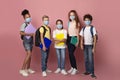 Education during virus outbreak. Diverse children with schoolbags and notebooks wearing masks on pink background