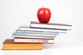 The educational books are stacked in the form of a ladder on the table and with a red juicy apple