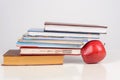 Educational books are stacked in the form of a ladder on the table, a red juicy apple supports a stack of books