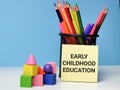 Phrase EARLY CHILDHOOD EDUCATION written on sticky note with colorful blocks and stationary.