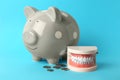 Educational dental typodont model, piggy bank and coins on light blue background. Expensive treatment Royalty Free Stock Photo