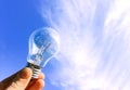 Eelectrical light bulb in hand on blue sky background. Hand holding light bulb on a background sky and sun. Royalty Free Stock Photo