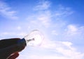 Eelectrical light bulb in hand on blue sky background. Hand holding light bulb on a background sky and sun. Royalty Free Stock Photo