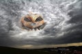An eerie halloween pumpkin head in the sky between thunderclouds looks at a city