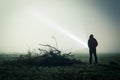 An eerie silhouette of a lone hooded figure in a field on a foggy night with a torch. With a dark edit