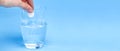 Effervescent instant tablet in a hand over a glass of water on a blue background. Banner with copy space. Treatment, vitamin Royalty Free Stock Photo