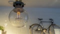 Efficient incandescent light bulb waste electricity against a tiled wall with a small bike and a plant pot. Royalty Free Stock Photo