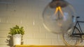 Efficient incandescent light bulb waste electricity against a tiled wall with a small bike and a plant pot. Royalty Free Stock Photo