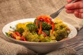 Egetable salad in a white ceramic bowl on a background of rough homespun fabric. A hand is stirring the salad with a fork. Close Royalty Free Stock Photo