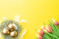 Egg color. Happy Easter decoration: golden colour eggs in basket with spring tulips white feathers on pastel yellow background. Royalty Free Stock Photo