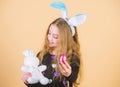 Egg feast. Little girl holding Easter egg and bunny toy. Cute child with Easter bunny rabbit bringing egg treat. Small