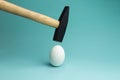 Egg and hammer hovering over it, before the hit. One egg and hammer on blue background Royalty Free Stock Photo