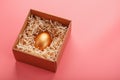 Egg made of gold in a wooden box on a pink background. The concept of exclusivity and superprize. Minimalistic composition