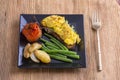 Egg omelette on a piece of black bread with red tomatoes, green beans and fried potato on a wooden table, close up. Breakfast conc Royalty Free Stock Photo