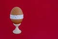 Egg standing on cup, on a soft red background. Easter egg tied with a festive ribbon Royalty Free Stock Photo