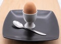 egg in a white cup with a spoon on a black plate on a wooden chopping board Royalty Free Stock Photo