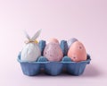 Egg wrapped in a paper in the shape of a bunny with colorful Easter eggs in carton tray. Minimal Easter concept Royalty Free Stock Photo