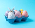 Egg wrapped in a paper in the shape of a bunny with colorful Easter eggs in carton tray. Minimal Easter concept Royalty Free Stock Photo