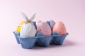 Egg wrapped in a paper in the shape of a bunny with colorful Easter eggs in carton tray. Minimal Easter concept Royalty Free Stock Photo