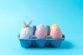 Egg wrapped in a paper in the shape of a bunny with colorful Easter eggs in carton tray. Minimal Easter concept Royalty Free Stock Photo