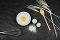 Egg yolk on flour, whisker and spoon on dark table