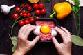 Egg yolk on minced pork in a black plate on a wooden table with cherry tomatoes, garlic, spices and mustard seeds. The Royalty Free Stock Photo