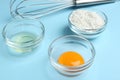 Egg yolk, white and flour in bowls on blue background, closeup