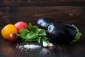 Eggplant (aubergine) with basil, garlic and tomatoes on dark wooden table. Fresh raw farm vegetables - harvest from the Royalty Free Stock Photo