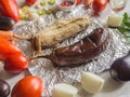 Eggplant baked on foil and vegetables are laid out on a wooden table. Vegetables on a light wooden background.