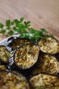 Eggplants baked with spices on plate with with bunch of parsley on wooden table, flat lay