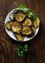 Eggplants baked with spices on plate with with bunch of parsley on wooden table, flat lay