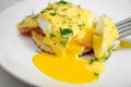 Eggs Benedict for breakfast on a white plate, liquid yolk