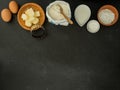 Eggs, butter, milk, sugar, baking powder, cutter and flour on slate background